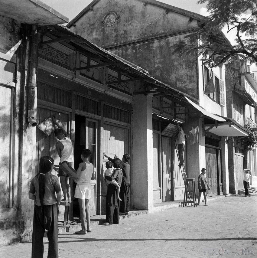 តាំងពីព្រឹកព្រលឹម ប្រជាជនហាណូយបានលើកទង់ជាតិ និងពាក្យស្លោកនៅមុខផ្ទះ ស្វាគមន៍ទាហានដែលបានរំដោះរដ្ឋធានី។ (រូបថត៖ បណ្ណសារ VNA) vna-potal-71-nam-giai-phong-thu-do-10101954-10102025-moc-son-ruc-ro-cua-nhan-dan-thu-do-153116793-8320151.jpg