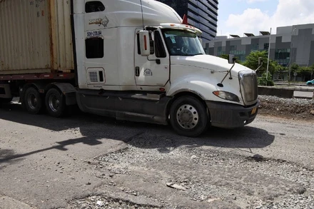 Xe tải lưu thông khó khăn giữa vòng vây ổ voi, ổ gà trên tuyến đường Nguyễn Văn Linh. (Ảnh: QUÝ HIỀN)