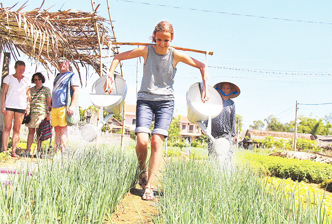 Một du khách nước ngoài thích thú tập gánh nước tưới vườn rau giữa trưa nắng. Ảnh: PHAN THÀNH