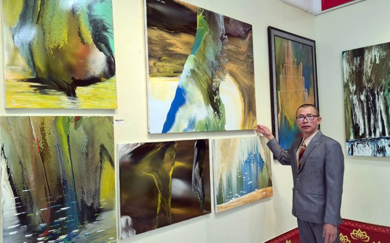 Họa sĩ Võ Trịnh Biện bên những tác phẩm của anh tại triển lãm.