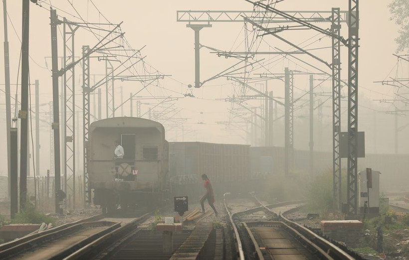 Một người phụ nữ băng qua đường ray khi tàu chở hàng chạy qua, vào một ngày sương mù ở New Delhi, Ấn Độ. Ảnh chụp ngày 12/11/2021. Ảnh: Reuters.