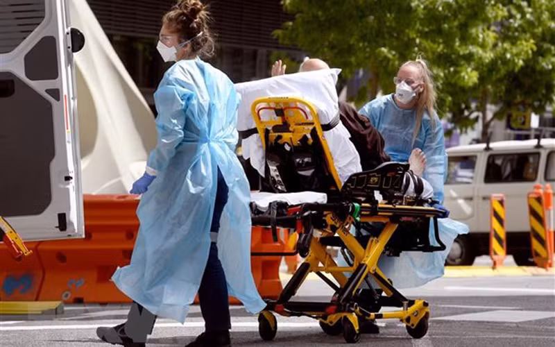 Nhân viên y tế chuyển bệnh nhân Covid-19 tới bệnh viện tại Melbourne, Australia. (Ảnh: AFP/TTXVN)