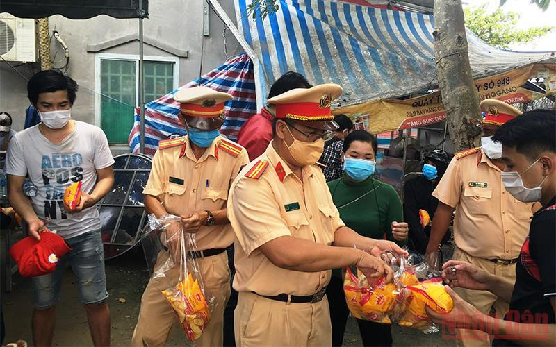Lực lượng công an phát bánh mì, nước uống cho bà con trong lúc chờ xe đến đón về địa phương cách ly theo quy định.
