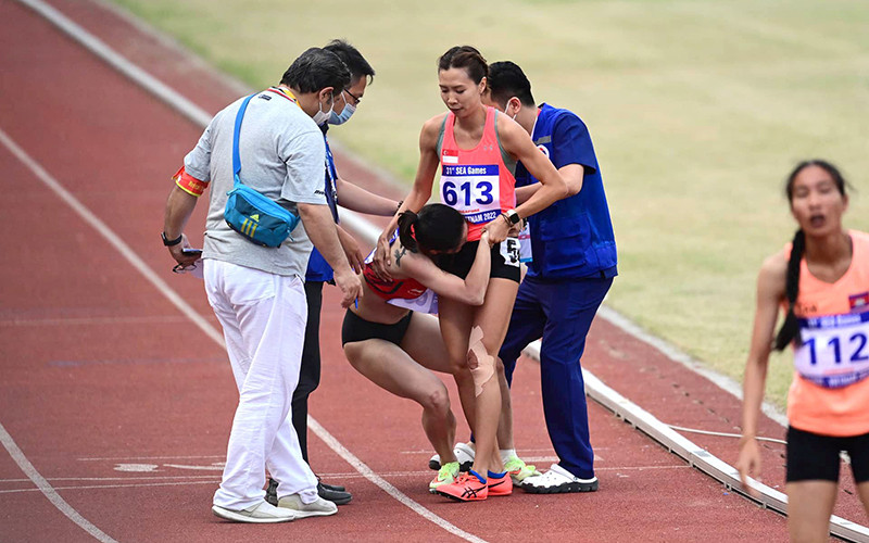 Vận động viên Singapore cùng nhân viên y tế đỡ Đinh Thị Bích sau cú vấp ngã đáng tiếc. (Ảnh THUẬN KHÁNH)