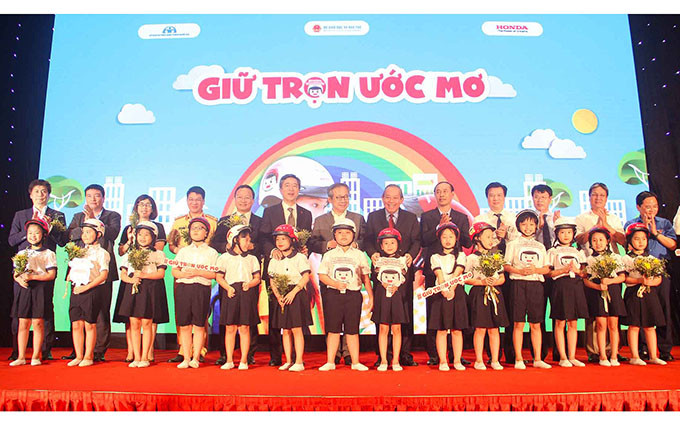 Phó Thủ tướng Trương Hòa Bình và các đại biểu trao tượng trưng mũ bảo hiểm đạt chuẩn cho các học sinh lớp một tại lễ công bố chương trình “Giữ trọn ước mơ” ngày 3-7.