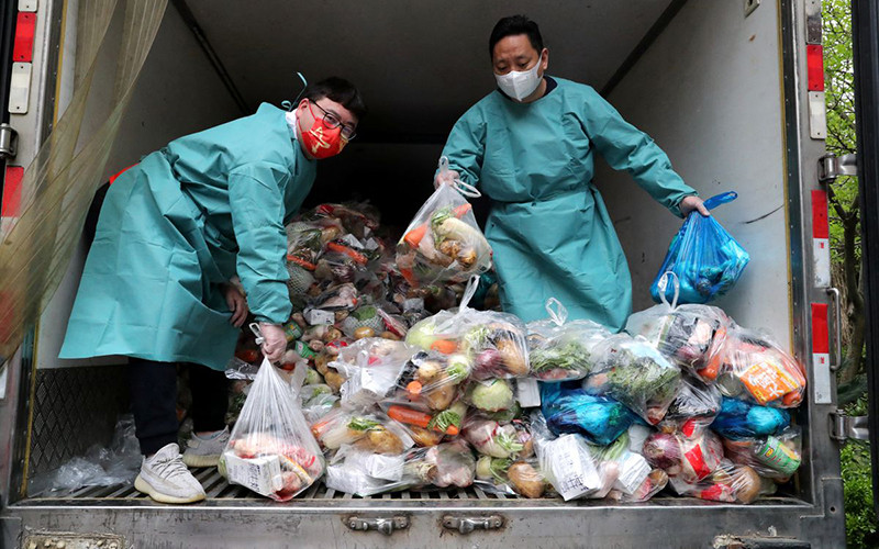 Nhân viên mặc đồ bảo hộ xếp thực phẩm lên xe tải để phân phát cho người dân. (Ảnh: China Daily)