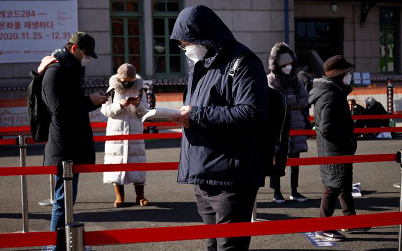 Một người đàn ông Hàn Quốc đọc sách trong khi chờ đến lượt xét nghiệm Covid-19 tại một khu vực xét nghiệm di động đặt trước nhà ga tàu ở Seoul dịp lễ Giáng sinh 2020. Ảnh: Reuters