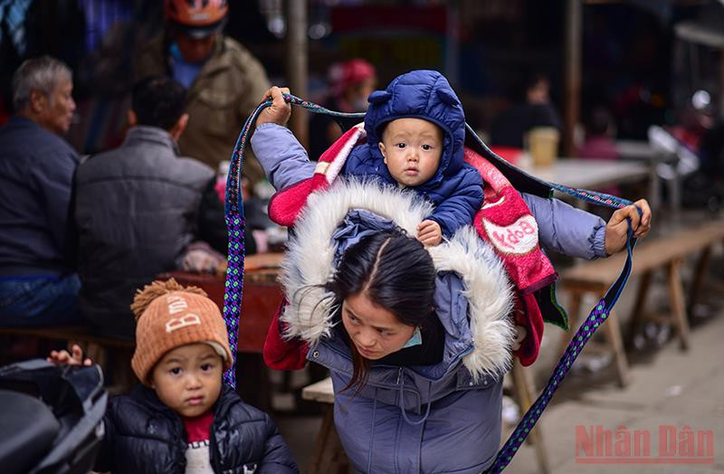 Khoảnh khắc người mẹ trẻ dân tộc H’ Mông quấn dây buộc địu con trên lưng tựa như cánh chim tung cánh che chở cho con. (Ảnh: Thành Đạt) 