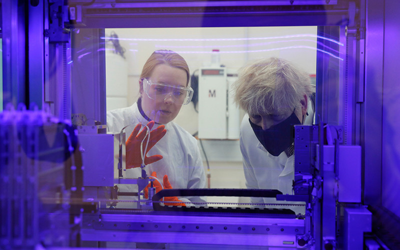 Thủ tướng Anh Boris Johnson (bên phải) đang quan sát máy xét nghiệm PCR (xét nghiệm virus SARS-CoV-2) cùng với nhà khoa học y sinh. Ảnh: AP.