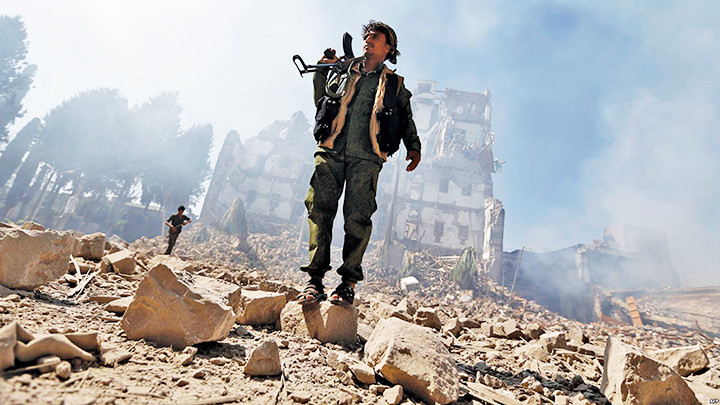 Một tay súng Houthi trước tòa nhà đổ nát sau trận không kích của liên quân Hồi giáo. Ảnh: ARAB NEWS