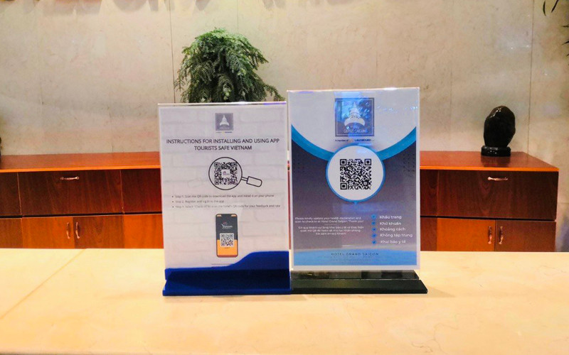 Thiết kế hướng dẫn khách du lịch tải và sử dụng ứng dụng “Du lịch Việt Nam an toàn” bằng 2 ngôn ngữ tiếng Việt – tiếng Anh tại quầy lễ tân của một khách sạn ở TP Hồ Chí Minh (Ảnh: Khách sạn cung cấp)