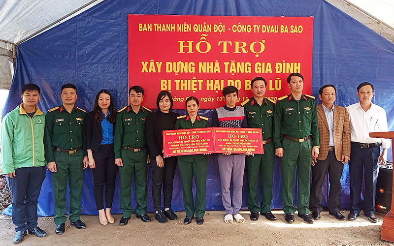 Sĩ quan dự bị Trần Hữu Diệu (áo xám trong ảnh) nhận nguồn hỗ trợ, động viên để xây dựng “Ngôi nhà 100 đồng” từ đại diện Ban Thanh niên quân đội ngay trên nền căn nhà cấp 4 vừa bị lũ cuốn trôi.