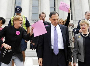 Ông Fuld tiếp tục bị truy vấn trên đường ra về sau buổi điều trần. Tờ bìa phía sau ông ghi từ "Kẻ lừa đảo" (ảnh: AP).