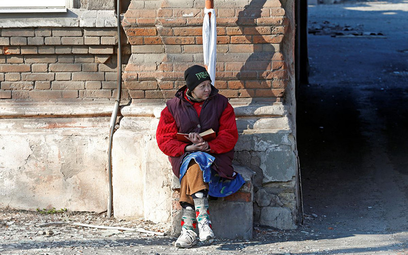 Người dân ngồi bên nhà một ngôi nhà bị hư hại do chiến sự tại Mariupol, Ukraine, ngày 7/4. (Ảnh: Reuters)