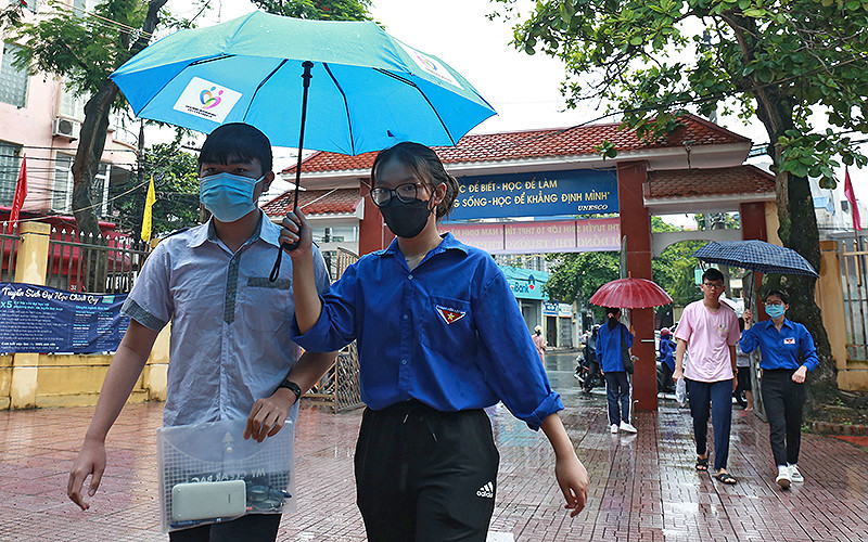 Các tình nguyện viên áo xanh che ô đưa từng thí sinh vào phòng thi tại điểm thi Trường Trung học phổ thông Nguyễn Khuyến (thành phố Nam Định).