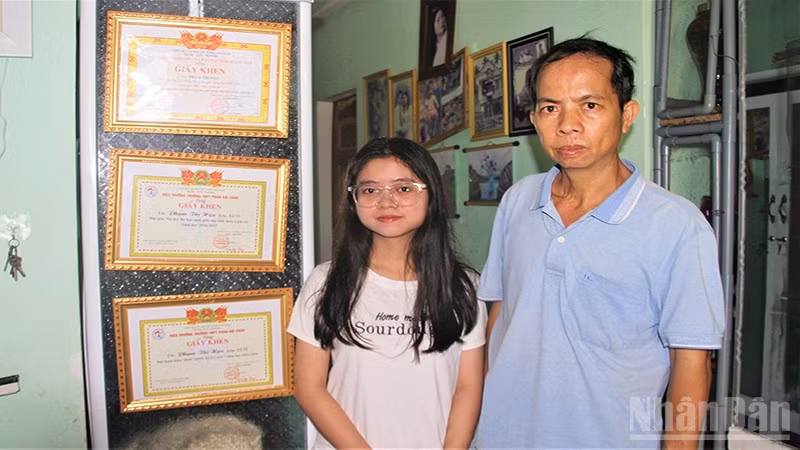 Em Phạm Thị Hậu và cậu ruột Ngô Thanh Đoàn đứng bên các thành tích học của em Hậu.