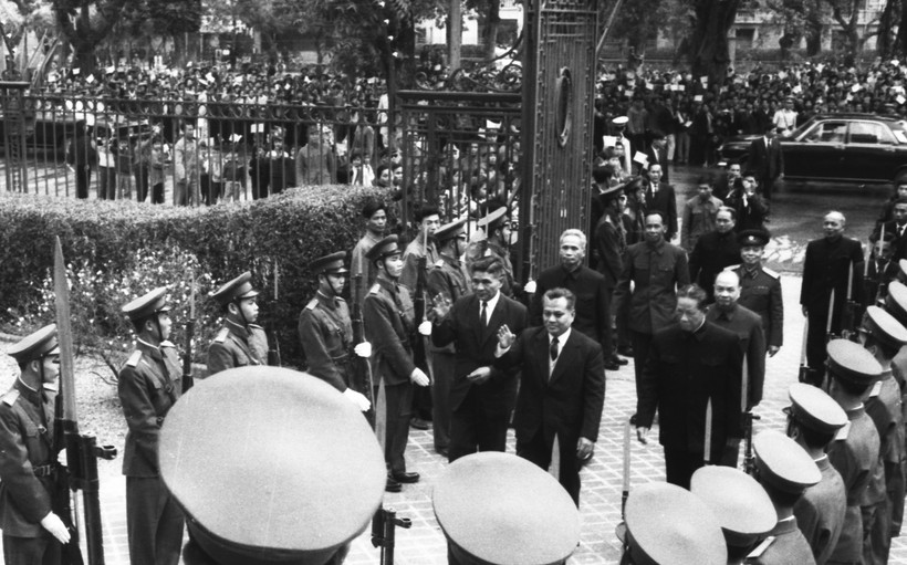 Đồng chí Kaysone Phomvihane đến Nhà khách Chính phủ 12 Ngô Quyền. Đi bên cạnh đồng chí Kaysone đồng chí Nouhak Phoumsavanh. Đón tiếp các đồng chí Lào là các đồng chí Tổng Bí thư Đảng Lao động Việt Nam Lê Duẩn, Thủ tướng Phạm Văn Đồng, Chủ tịch Quốc hội Trường Chinh. Phía sau là đông đảo nhân dân Hà Nội tập trung chào đón.