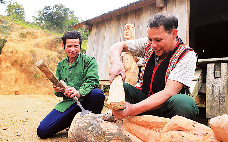 Nghệ nhân Ưu tú A Gông (bên phải) đang truyền dạy lại kỹ năng tạc tượng cho người dân trong làng.