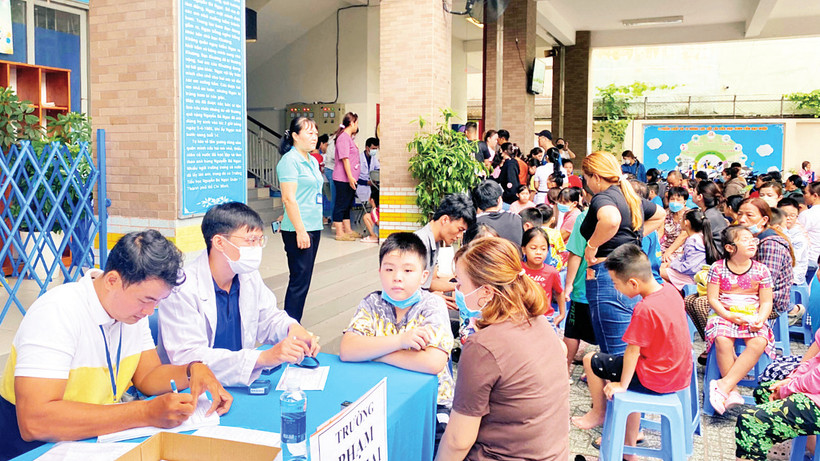 Phụ huynh và học sinh xếp hàng tại điểm tiêm ở Trường tiểu học Âu Cơ, Quận 11 để đợi tiêm vắc-xin sởi. 