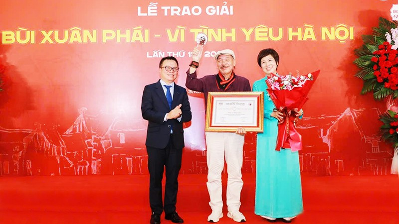 Nhà báo Lê Quốc Minh, Ủy viên Trung ương Đảng, Tổng Biên tập Báo Nhân Dân, Phó Trưởng ban Tuyên giáo và Dân vận Trung ương, Chủ tịch Hội Nhà báo Việt Nam và nhà báo Vũ Việt Trang, Tổng Giám đốc TTXVN trao Giải thưởng Lớn - Vì tình yêu Hà Nội cho nhạc sĩ Trần Tiến. Ảnh: PHAN PHƯƠNG