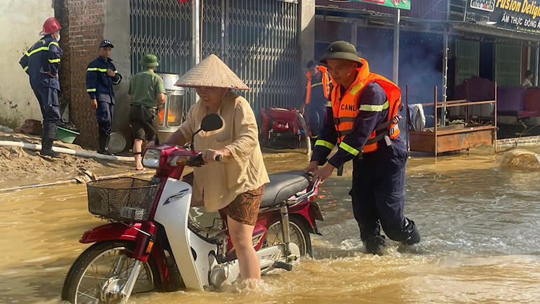 Chiến sĩ công an giúp người dân di chuyển an toàn vùng ngập lụt. (Ảnh: Thùy Dương)