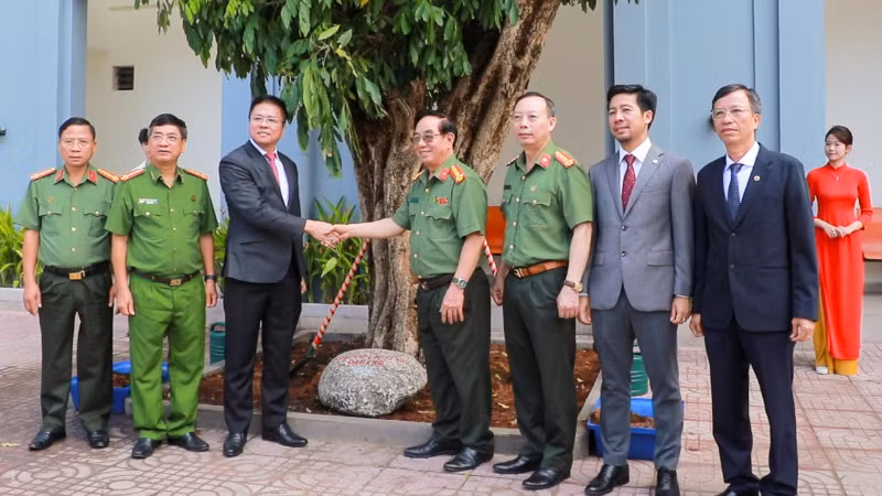 Lãnh đạo nhà trường và đại diện đoàn công tác chụp ảnh bên cây nhãn trồng lưu niệm. 