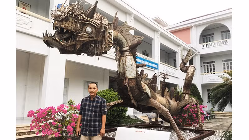 Họa sĩ Đinh Thanh Hải bên tác phẩm “Con rồng sắt” của nhà điêu khắc Pháp Marc Morvan, làm bằng phế liệu vỏ bom đạn, inox sau chiến tranh, hiện đặt tại sân Trường đại học Khánh Hòa.