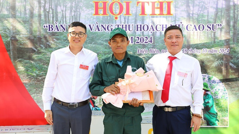 Công nhân, quần chúng ưu tú Lò Văn Thiệp (ở giữa) thuộc nông trường cao su Mường Chà vinh dự được các đồng chí lãnh đạo Công ty cổ phần cao-su Điện Biên tặng hoa chúc mừng đoạt kiện tướng "bàn tay vàng thu hoạch mủ cao-su".