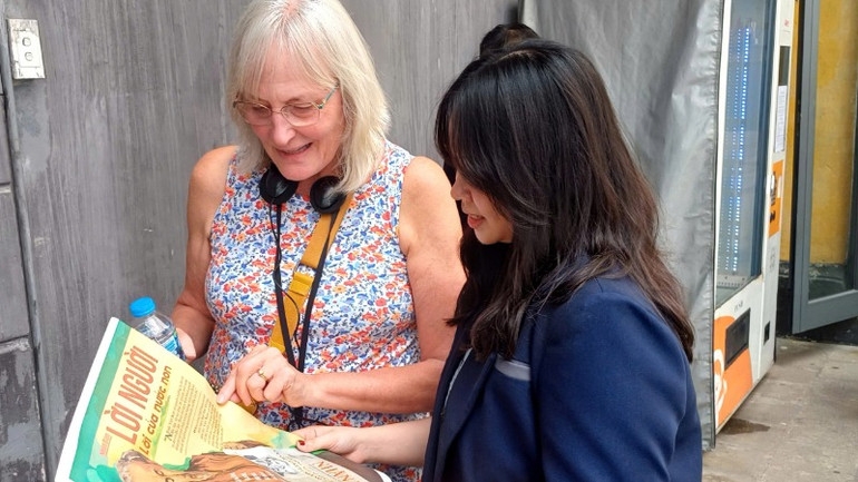 Một phụ huynh học sinh đang giới thiệu với du khách nước ngoài về ấn phẩm của Báo Nhân Dân.