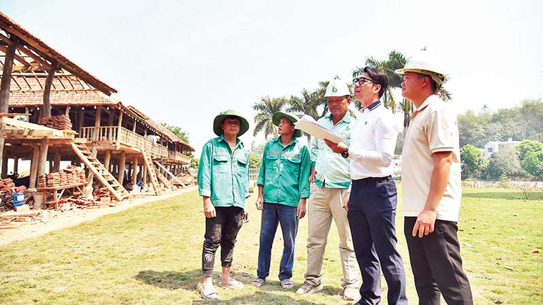 Anh Bùi Anh Tiến (người đeo kính) trao đổi với công nhân thi công dãy nhà sàn của người Thái cổ. (Ảnh MỸ HÀ)