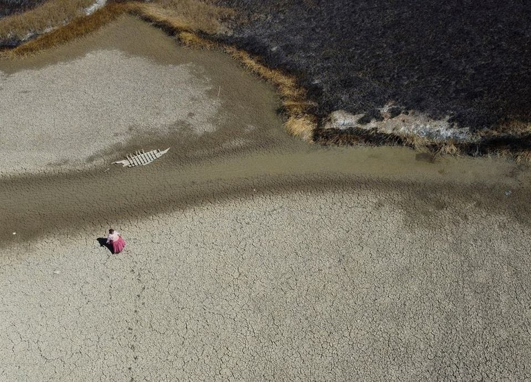 Bà Isabel Apaza đi trên lòng hồ Titicaca khô nứt bên cạnh một chiếc thuyền bỏ hoang. Ảnh: Reuters