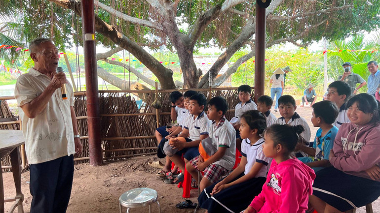 Cựu chiến binh Huỳnh Minh Ê đọc thơ Lục Vân Tiên cho các em học sinh nghe khi đến điểm du lịch sinh thái của mình.