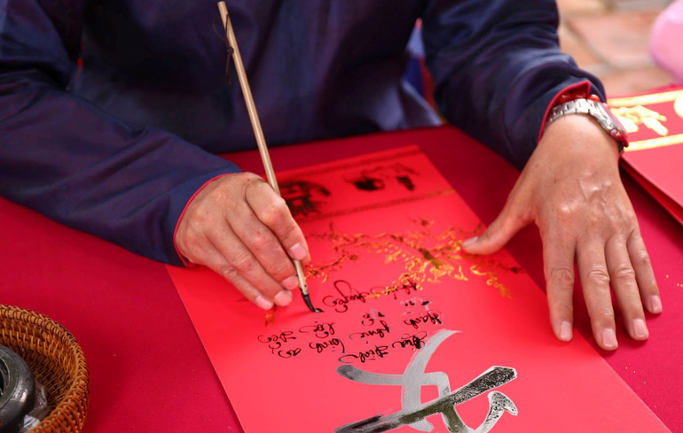 Thầy đồ viết chữ thư pháp cho khách tham quan. (Ảnh: Uyển Nhi)