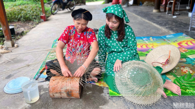 Bà Hoàng Thị Huệ (bên trái) trò chuyện và hướng dẫn khách làm nón.