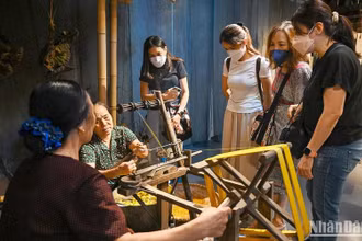 Du khách nước ngoài tìm hiểu về nghề ươm tơ, dệt vải truyền thống tại triển lãm “Muôn nẻo đường tơ”. (Ảnh DUY ĐĂNG)