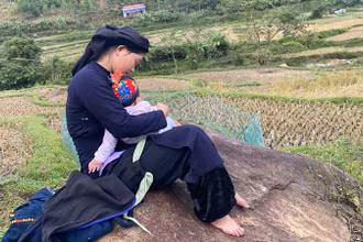 Những đứa trẻ được nghe mẹ hát ru khi theo mẹ đi làm. (Trong ảnh: Một phụ nữ ở xã Giáo Hiệu hát ru trẻ khi đi làm đồng). (Ảnh: THU TRANG)
