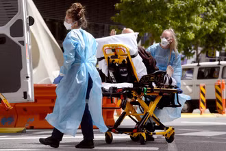 Nhân viên y tế chuyển bệnh nhân Covid-19 tới bệnh viện tại Melbourne, Australia. (Ảnh: AFP/TTXVN)