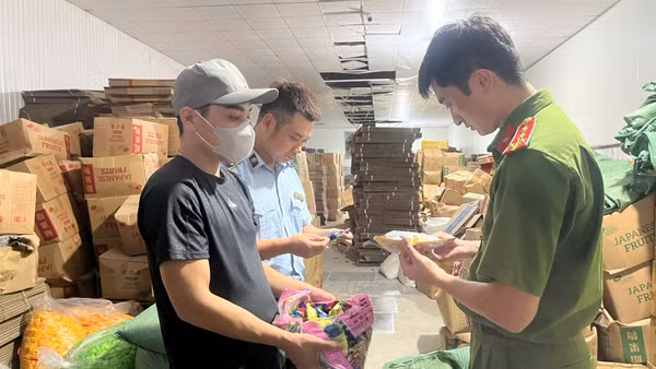 Lực lượng chức năng kiểm tra địa điểm sản xuất kinh doanh bánh, kẹo, nước uống do Nguyễn Quang Đạt (đeo khẩu trang) làm chủ. (Ảnh: Công an Hà Nội)