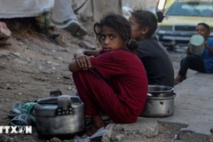 Trẻ em ngồi chờ nhận thức ăn cứu trợ ở thành phố Gaza. (Ảnh: THX/TTXVN)