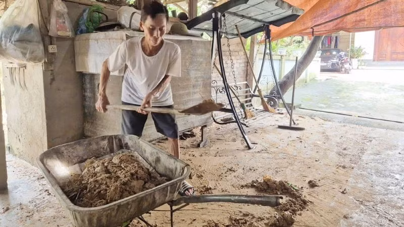 Ông Bùi Văn Nghiếp, tổ dân phố Sơn Hải thu dọn bùn đất còn đọng lại trên sân nhà. (Ảnh: TRỊNH LAN)