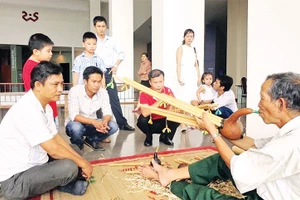 Nghệ nhân Ama Hloan ở buôn Akô Dhông, phường Buôn Ma Thuột, tỉnh Đắk Lắk giới thiệu nhạc cụ Đinh Năm với du khách.