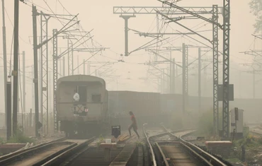 Một người phụ nữ băng qua đường ray khi tàu chở hàng chạy qua, vào một ngày sương mù ở New Delhi, Ấn Độ. Ảnh chụp ngày 12/11/2021. Ảnh: Reuters.