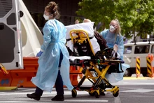Nhân viên y tế chuyển bệnh nhân Covid-19 tới bệnh viện tại Melbourne, Australia. (Ảnh: AFP/TTXVN)