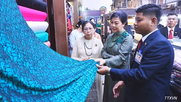 Phu nhân Ngô Phương Ly và Phu nhân Kyu Kyu Hla tham quan khu trưng bày sản phẩm lụa truyền thống và giới thiệu các sản phẩm đặc sắc của làng nghề Vạn Phúc. (Ảnh: TTXVN)