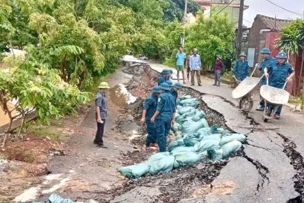 Lực lượng dân quân của xã Lệ Thủy chuyển bao cát đắp vào đoạn đường bị sụt lún trong khi nước sông Kiến Giang đang dâng cao. (Ảnh: LT) 