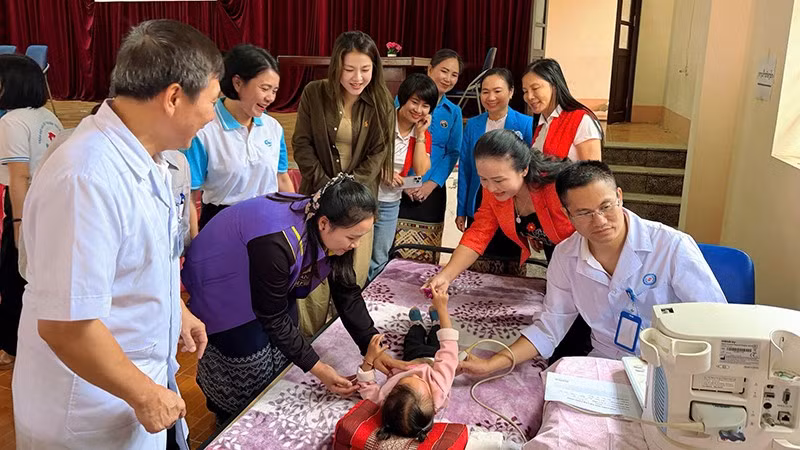 Phụ nữ cùng bác sĩ chăm sóc, khám bệnh cho trẻ em Lào.