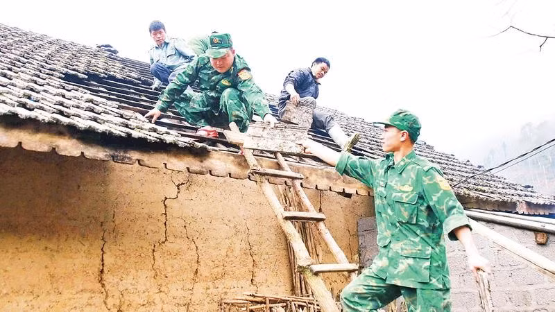 Cán bộ, chiến sĩ Đồn Biên phòng Tùng Vài giúp gia đình chị Hầu Thị Mái, thôn Lùng Khố lợp lại mái nhà bị hư hỏng sau thiên tai.