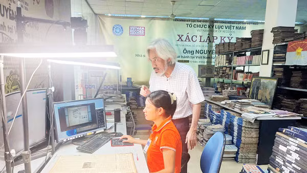 Nhà sưu tập Nguyễn Phi Dũng hướng dẫn chị Nguyễn Thị Hồng thực hiện việc chụp các trang Báo Nhân Dân. (Ảnh: MẠNH HÀO)