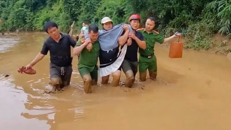 Công an xã Hữu Kiệm dìu sản phụ Kha Thị May vượt bùn lũ đến trạm y tế. (Ảnh: NGÔ HÙNG)
