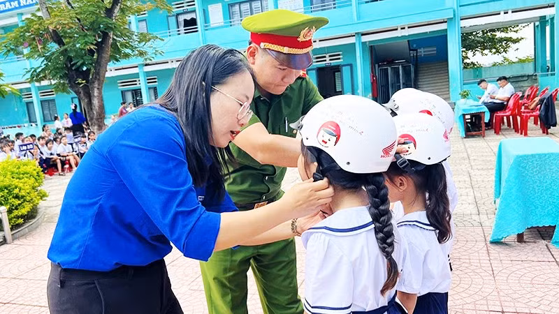 Giáo viên và cán bộ Công an hướng dẫn học sinh đội mũ bảo hiểm đúng cách.